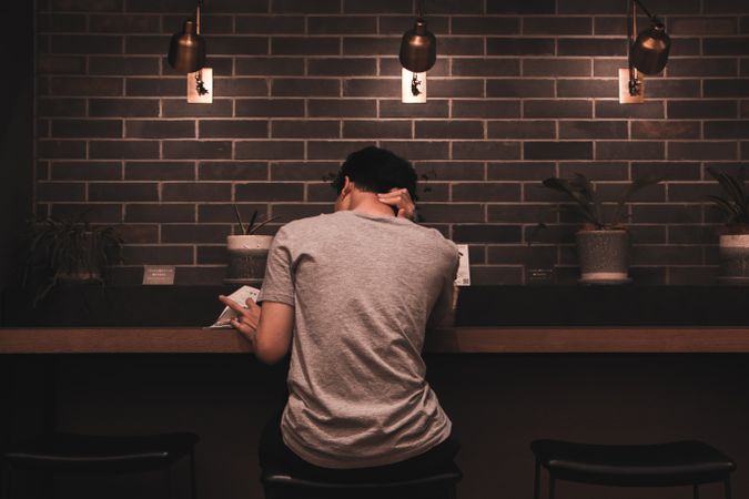 Back view of young man sitting at a high table reading a book