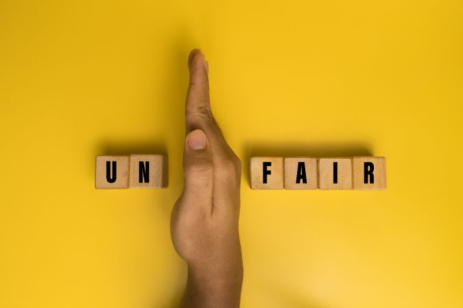 male hand put away first two letter from unfair word to be read fair isolated on yellow background. fairness concept
