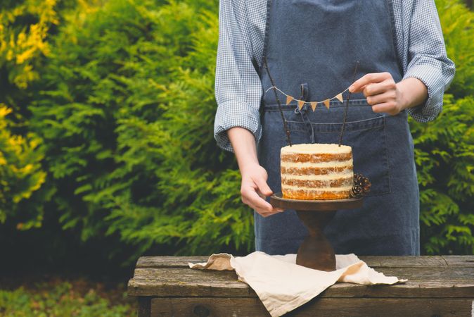 Man in blue apron decorating cake outside