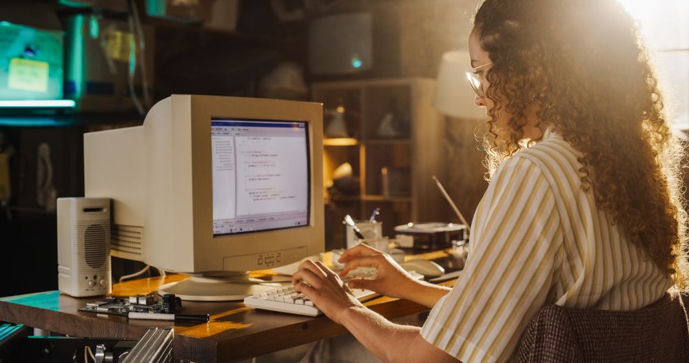 Side View Of Hispanic Female Engineering Student Writing Academic Thesis On Old Desktop Computer In Retro Garage.