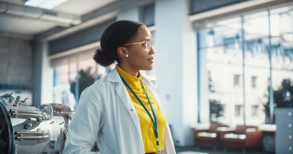 Portrait of Young Dreamy Black Woman Wearing Glasses and a Lab Coat, Looking Out Of Window.