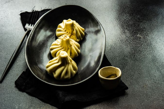 Plate of three Georgian khinkali dumplings on dark table