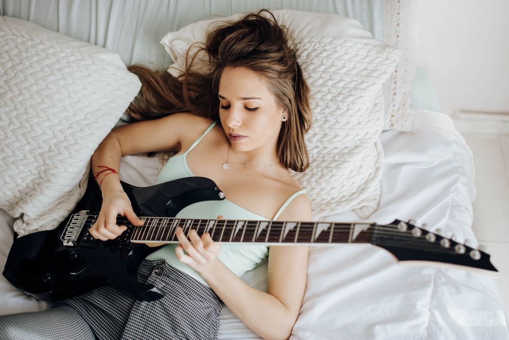 Young brunette woman playing guitar on bed
