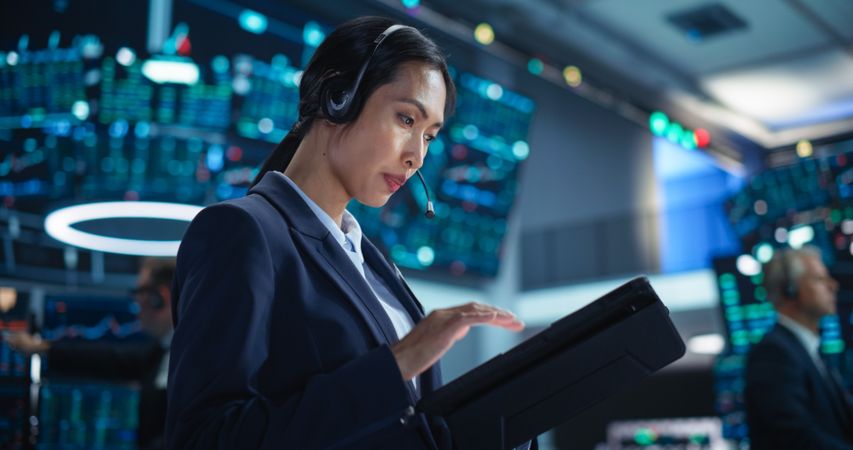 Female Investment Banker Wearing Headphones and Using a Tablet Computer with Financial Market Analytics Data.