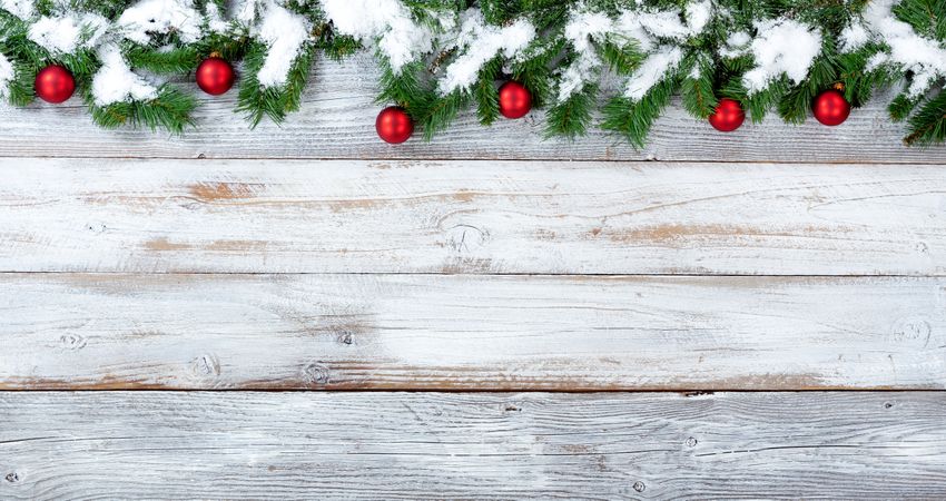 Snowy Christmas evergreen branches and red ornaments on vintage wooden planks