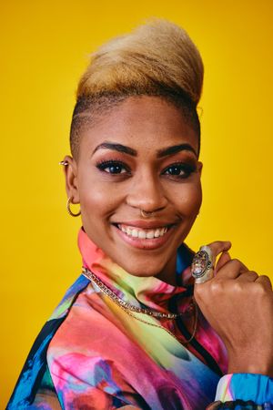 Happy Black woman in bright 80s windbreaker jacket in yellow studio
