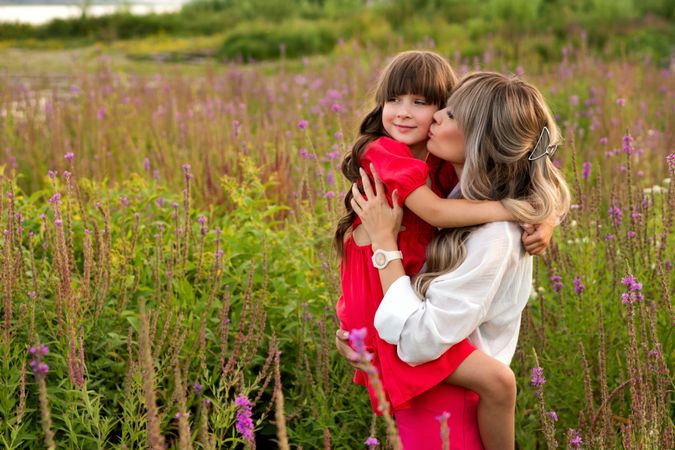 Mom and little daughter walking among meadow flowers
