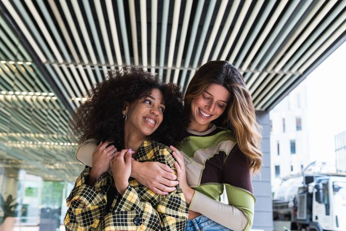 Young happy multiethnic girlfriends embracing against glass wall