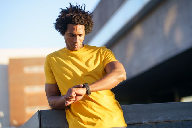 Black man in yellow t-shirt checking his smart watch in the sun