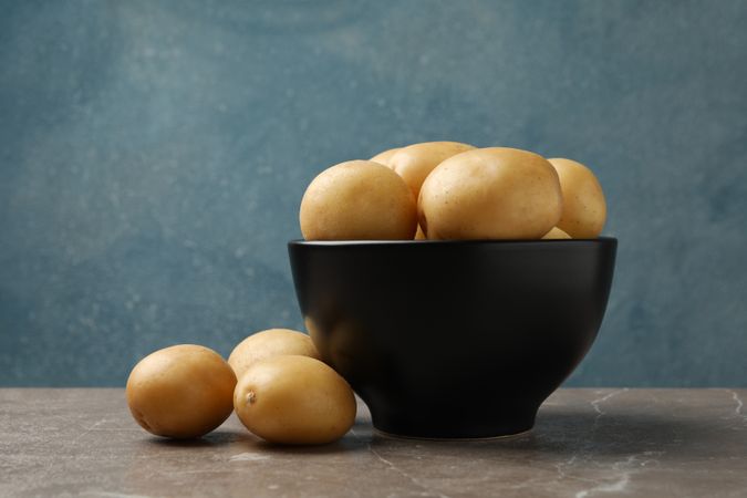 Side view of dark bowl full of potatoes, copy space
