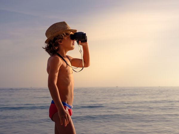 Boy enjoying seascape through binoculars at sunset