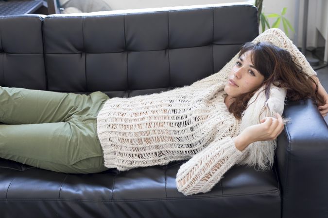 Female in wooly sweater daydreaming on leather couch in living room