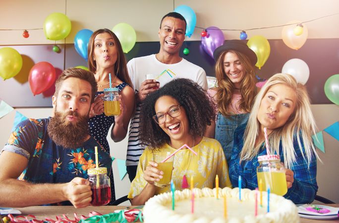 Friends smiling with drinks, balloons and birthday cake with candles