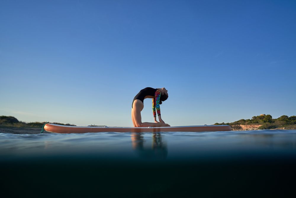 Slim woman practicing yoga in Camel pose on paddleboard in sea