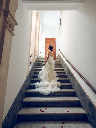 Newlywed woman in elegant wedding dress strolling upstairs with