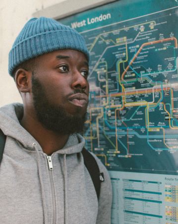 Man with knit cap standing beside subway map
