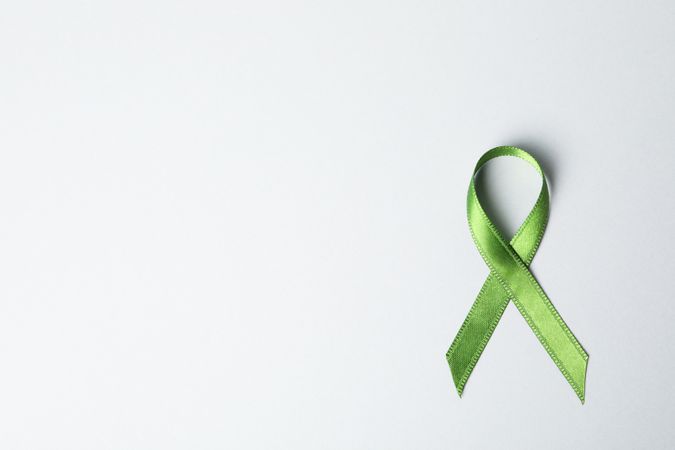 Green awareness ribbon on grey background, space for text