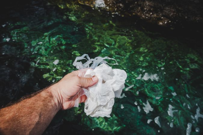 Crop man pulling plastic bag out of water