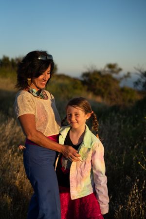 Portrait of young girl smiling and looking at camera standing by her mother with tall grass behind