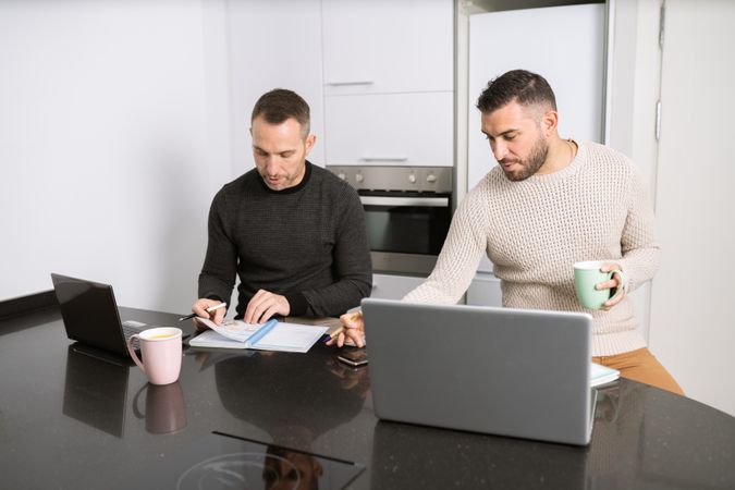 Two men working on laptops from their kitchen counter