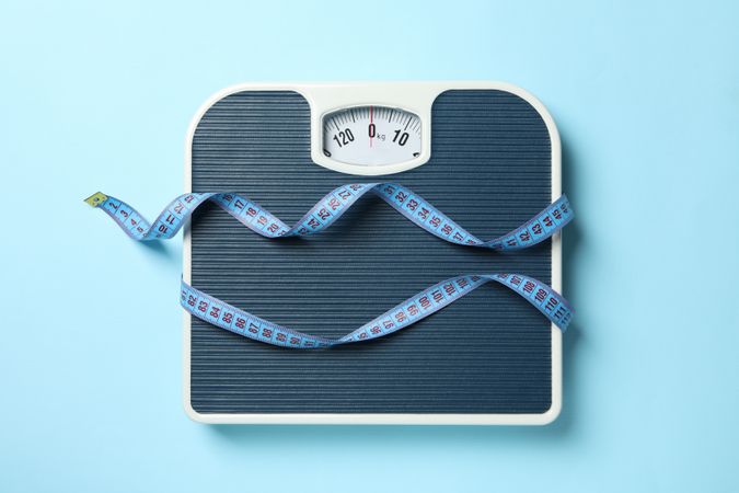 Scales and measuring tape on blue background. Weight loss concept