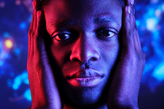 Upset Black man touching face in dark studio
