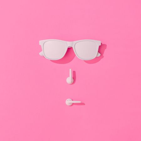 Summer objects of sunglasses and EarPods making face on pink background