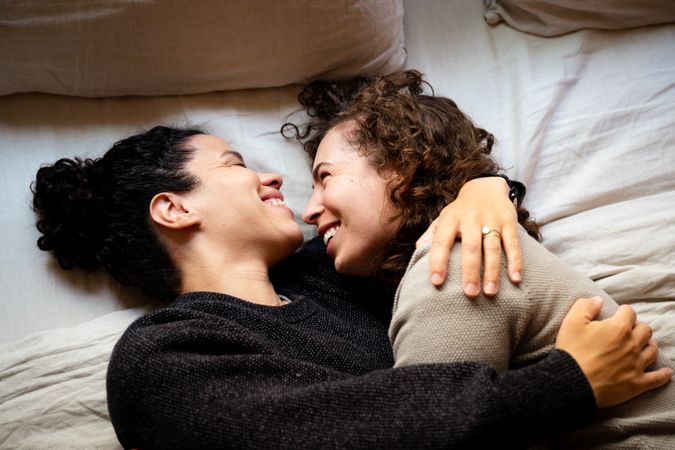 Two women lying down holding each other on bed in loving hug