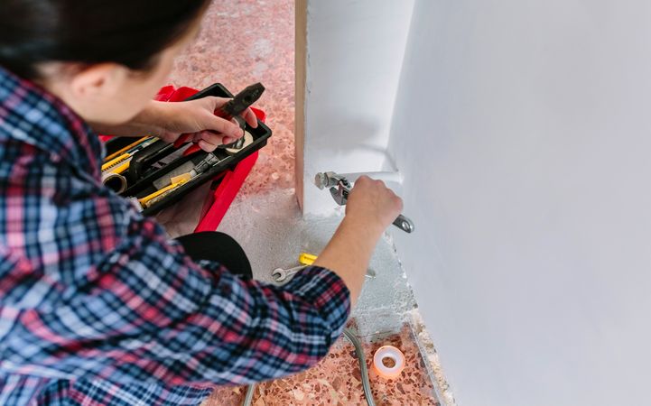 Female plumber tightening pipe with wrench in heating installation