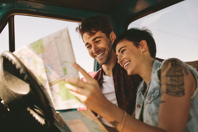 Youthful couple discussing trip details while looking at map in truck