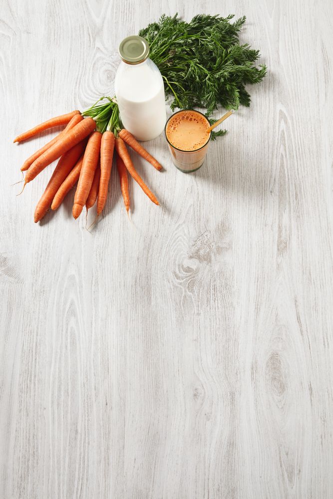 Top view of carrot juice with bunch of carrots and bottle of milk with copy space