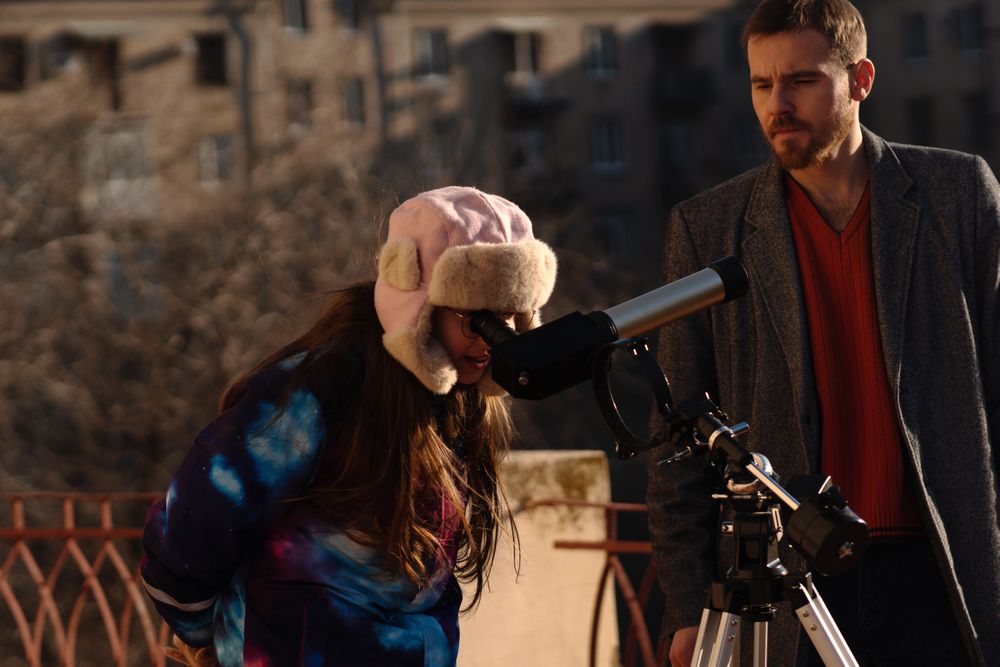 Girl and instructor use tripod-mounted telescope for rooftop solar study