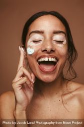 Portrait of young woman with vitiligo applying cream on cheek 0yYd10