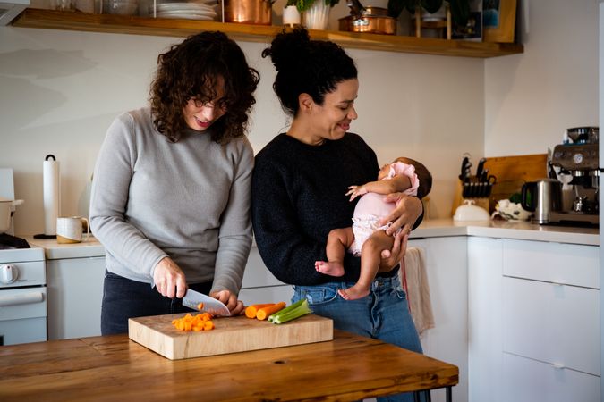 Happy female couple and baby in kitchen chopping vegetables