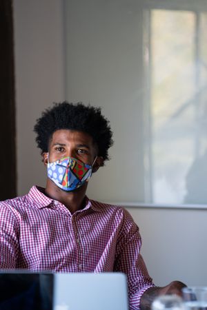 Man sitting in a modern office wearing a brightly colored face mask