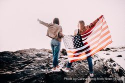 Two young women holding the American flag outside standing atop rocks E4Agm0