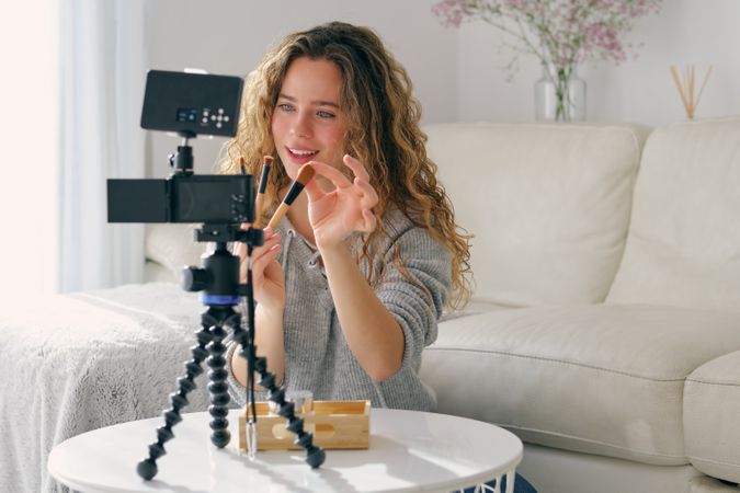 Female blogger holding different cosmetic brushes in front of camera