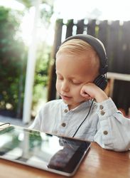 Blond boy using headphones and watching show on digital tablet, vertical