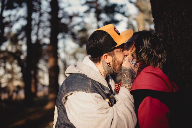 Happy couple hugging and kissing near tree in park