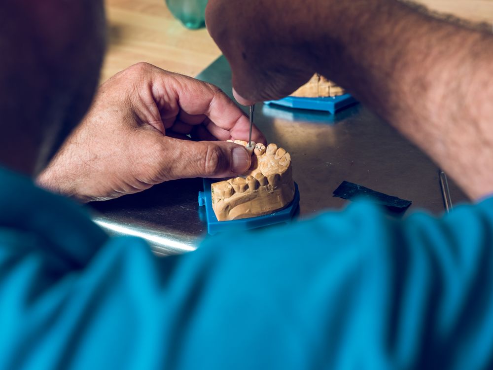 Crop dental technician inserting teeth into denture