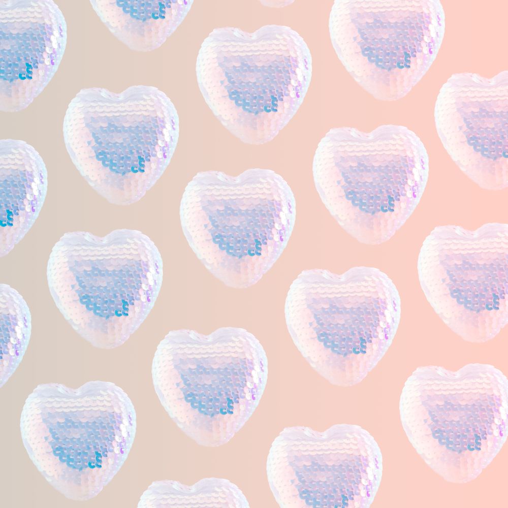 Pattern of iridescent sequins hearts on pink background