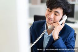 Calm Asian male in suit on satisfying phone call at work 0vBzR0