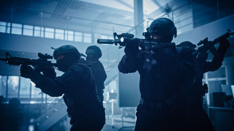 Close Up Portraits of Masked Squad of Armed SWAT Police Officers Storm a Dark Seized Office Building with Desks and Computers.