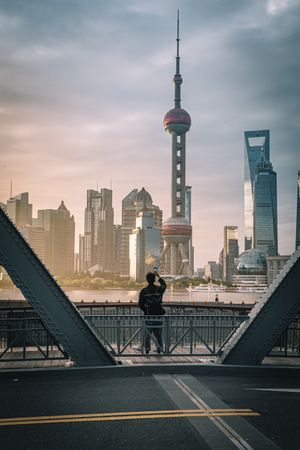 Back view of man standing by shoreline of Huangpu river in Shanghai, China at sunset
