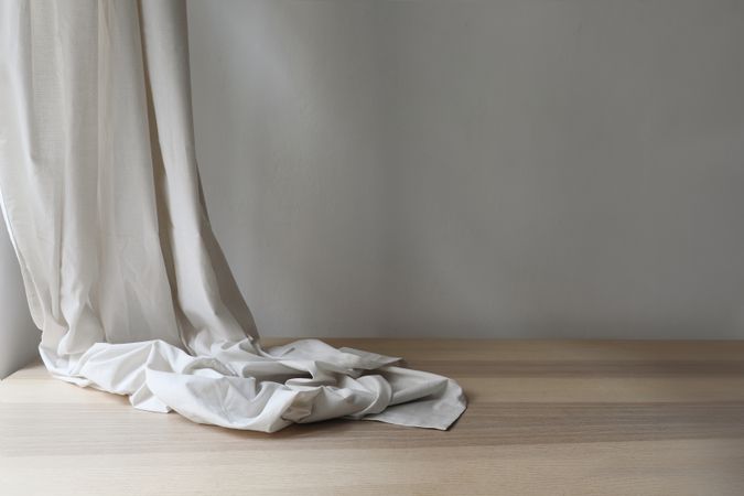 Decorative grey linen curtain, folded drapery and wooden table, floor. Empty wall background. Aesthetic sunlight shadows. Minimalist template for home room interior product, copy space.