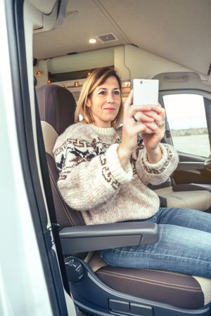 Female in cozy sweater taking picture with phone