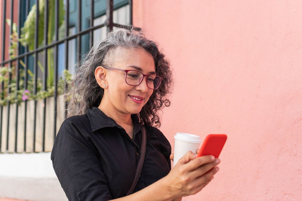 Hispanic woman sending message on cellphone while walking in the urban environment.