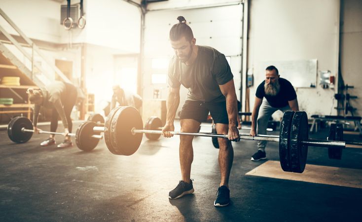 Healthy man lifting heavy in busy gym