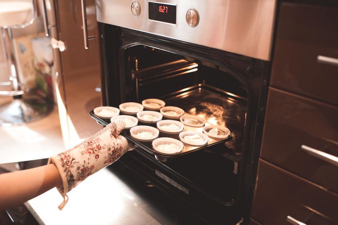 Cropped image of person putting cupcakes in the oven