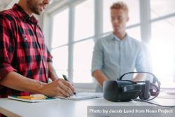 Shot of two young man standing at a table with VR goggles writing on notepad 5R1VB0